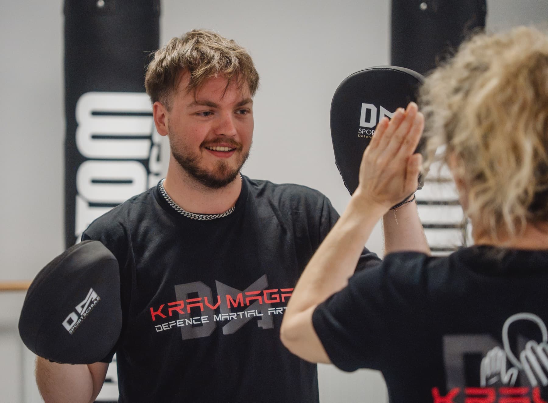 Lächelnder Trainer hält die Pratzen für eine Teilnehmerin
